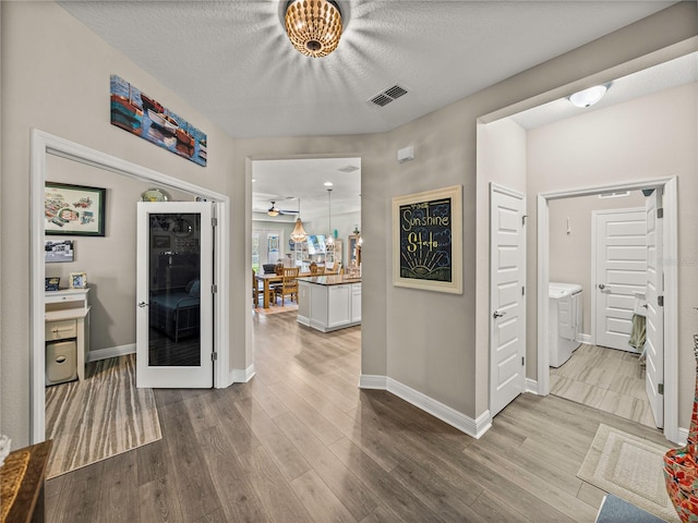 hallway featuring independent washer and dryer, a textured ceiling, and wood-type flooring