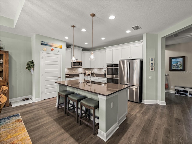 kitchen featuring dark hardwood / wood-style floors, a center island with sink, sink, white cabinets, and appliances with stainless steel finishes