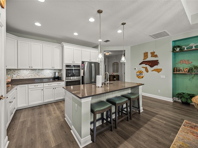 kitchen with an island with sink, a kitchen breakfast bar, dark hardwood / wood-style flooring, white cabinetry, and stainless steel appliances