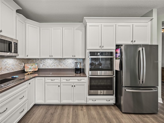 kitchen with appliances with stainless steel finishes, white cabinetry, a textured ceiling, and dark hardwood / wood-style flooring