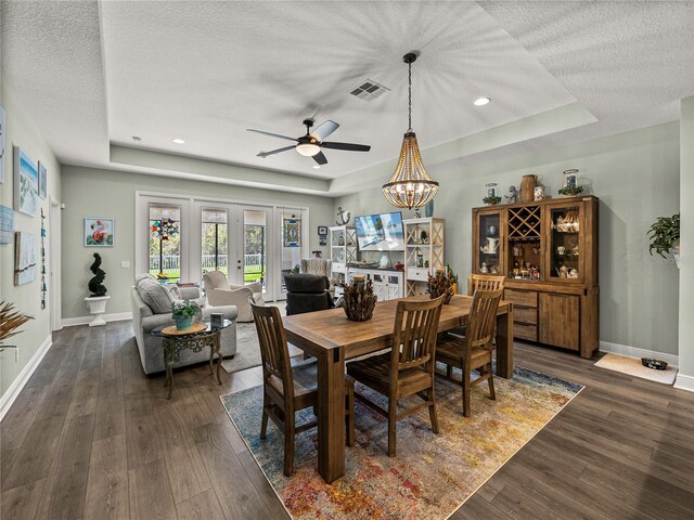 dining area with ceiling fan with notable chandelier, a raised ceiling, a textured ceiling, and dark hardwood / wood-style floors