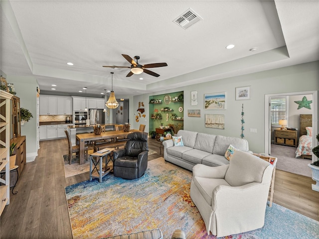 living room with light hardwood / wood-style floors, a raised ceiling, and ceiling fan