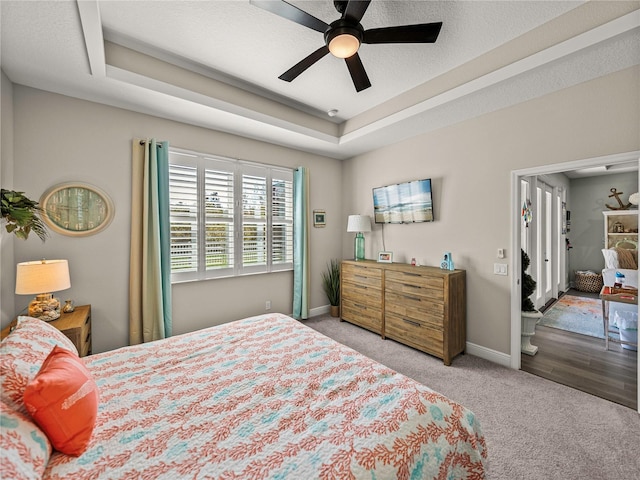 bedroom featuring ceiling fan, a textured ceiling, a tray ceiling, and light colored carpet