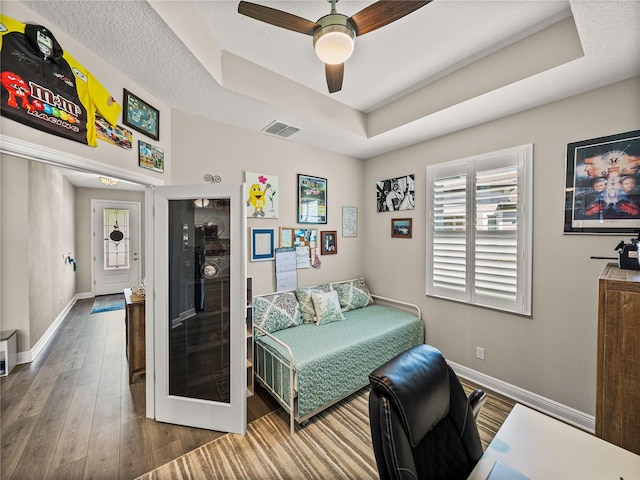 bedroom featuring ceiling fan, a raised ceiling, a textured ceiling, and hardwood / wood-style floors