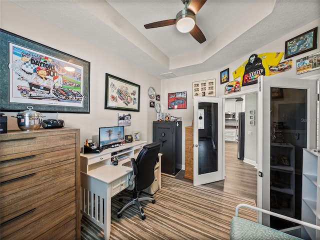 office space with a textured ceiling, hardwood / wood-style flooring, a tray ceiling, and ceiling fan