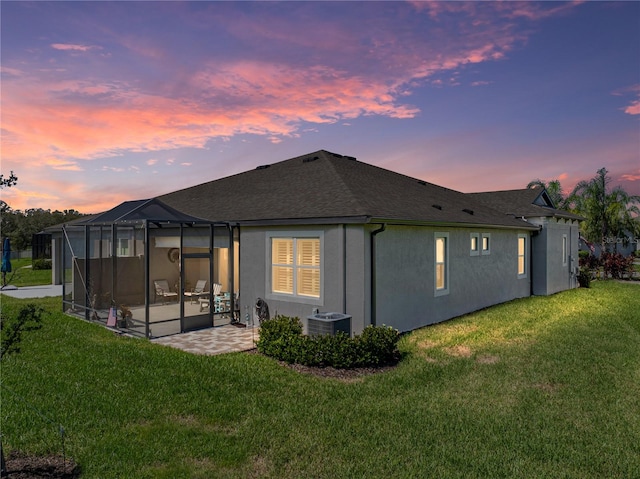 back house at dusk featuring central AC, a yard, a patio area, and a lanai