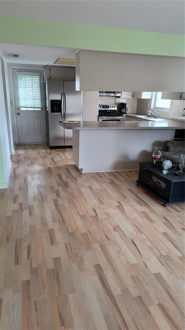 kitchen featuring extractor fan, kitchen peninsula, stainless steel appliances, and light wood-type flooring