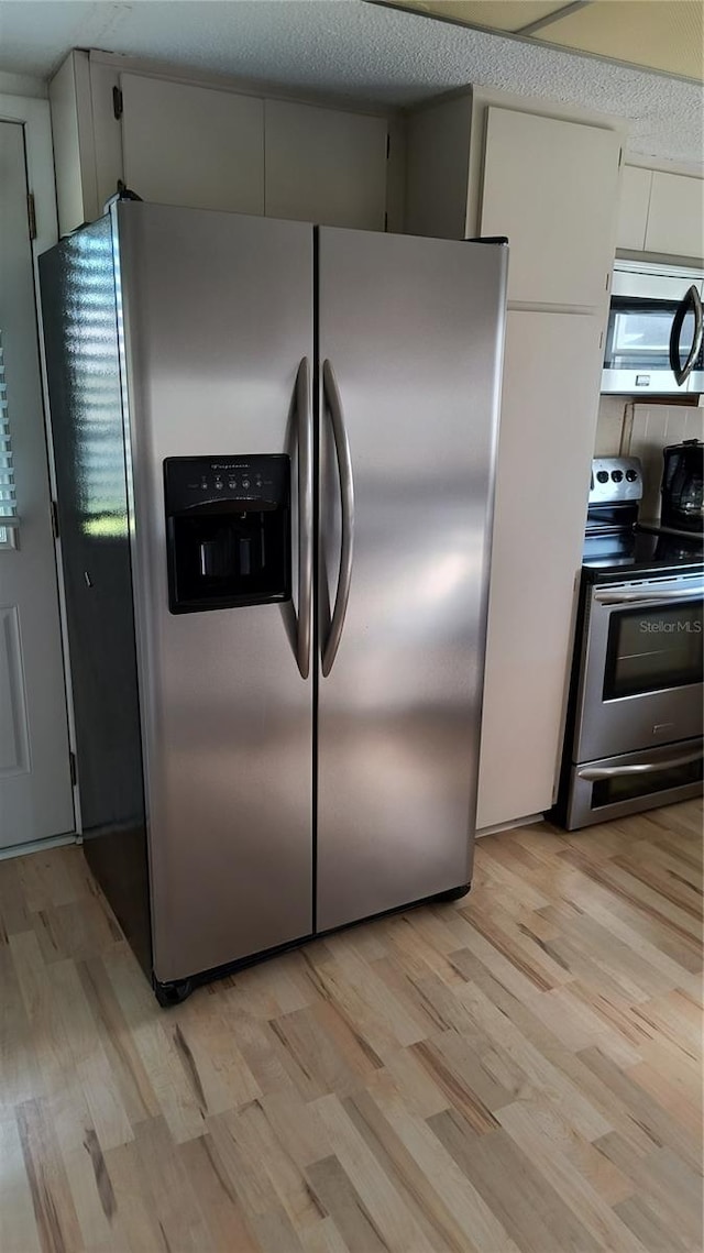 kitchen with appliances with stainless steel finishes, white cabinets, and light wood-type flooring