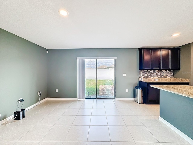 kitchen featuring light tile patterned flooring, dark brown cabinets, light stone countertops, and tasteful backsplash