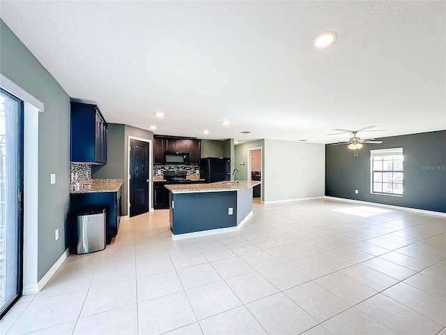 kitchen featuring black appliances, tasteful backsplash, an island with sink, light tile patterned flooring, and ceiling fan