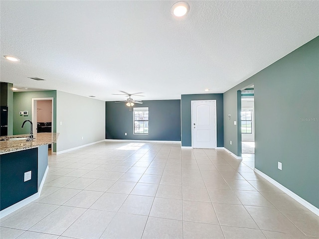 unfurnished living room featuring a wealth of natural light, ceiling fan, a textured ceiling, and sink