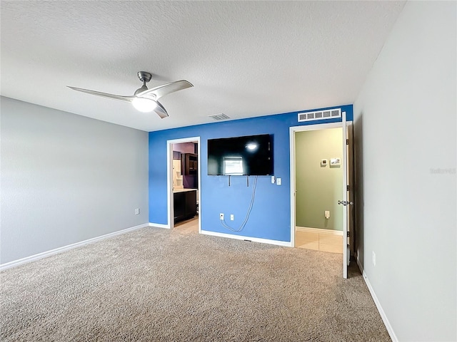 unfurnished bedroom with a textured ceiling, light colored carpet, ceiling fan, and ensuite bathroom