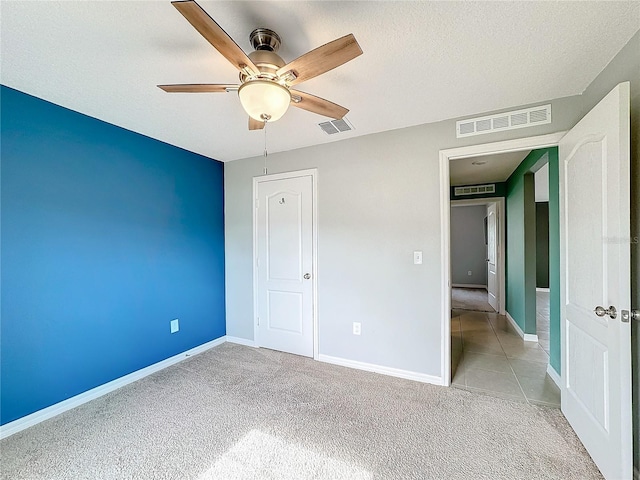 unfurnished bedroom featuring a textured ceiling, light colored carpet, ceiling fan, and a closet