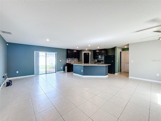 kitchen with a textured ceiling, decorative backsplash, light tile patterned flooring, and a kitchen island with sink