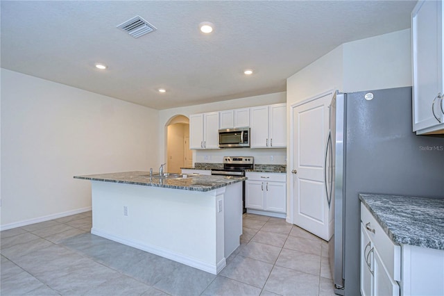 kitchen featuring white cabinets, dark stone countertops, stainless steel appliances, and a kitchen island with sink