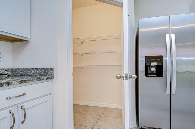 kitchen featuring stone counters, stainless steel fridge, white cabinets, and light tile patterned floors