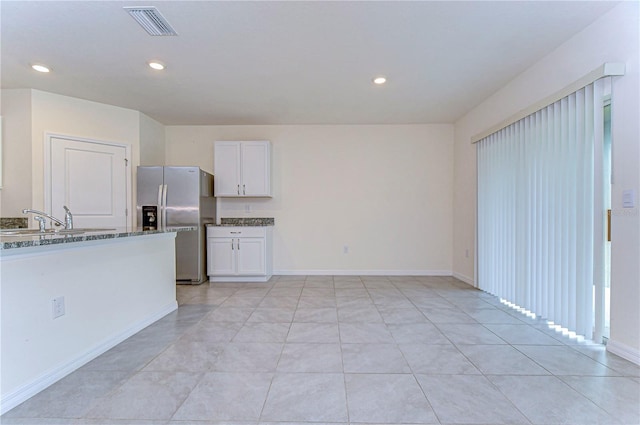 kitchen featuring dark stone counters, sink, stainless steel fridge with ice dispenser, light tile patterned floors, and white cabinetry