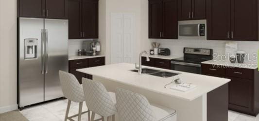 kitchen with appliances with stainless steel finishes, an island with sink, a breakfast bar, dark brown cabinetry, and sink