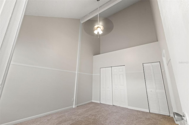 unfurnished bedroom featuring high vaulted ceiling, beam ceiling, carpet flooring, and multiple closets