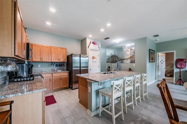 kitchen featuring appliances with stainless steel finishes, a kitchen breakfast bar, light stone countertops, light wood-type flooring, and sink