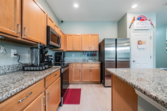 kitchen with light stone counters, appliances with stainless steel finishes, and light hardwood / wood-style floors