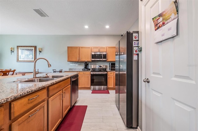 kitchen featuring light stone counters, a textured ceiling, sink, light hardwood / wood-style floors, and stainless steel appliances