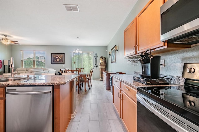 kitchen featuring hanging light fixtures, appliances with stainless steel finishes, light hardwood / wood-style flooring, ceiling fan with notable chandelier, and light stone counters