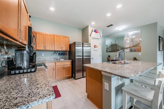 kitchen with light wood-type flooring, appliances with stainless steel finishes, a kitchen bar, and light stone counters