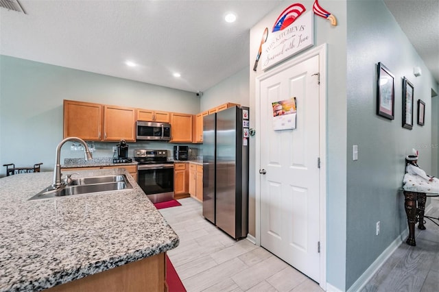 kitchen featuring sink, light stone countertops, light wood-type flooring, appliances with stainless steel finishes, and a textured ceiling