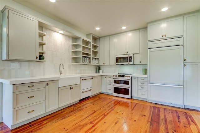 kitchen with tasteful backsplash, stainless steel range, sink, paneled built in refrigerator, and light hardwood / wood-style floors