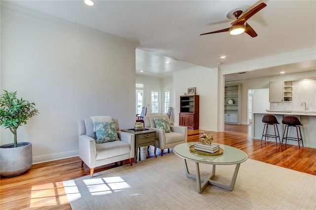 living room featuring light wood-type flooring, ceiling fan, crown molding, and sink