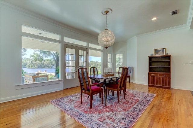 dining room featuring french doors, a water view, crown molding, hardwood / wood-style flooring, and a chandelier