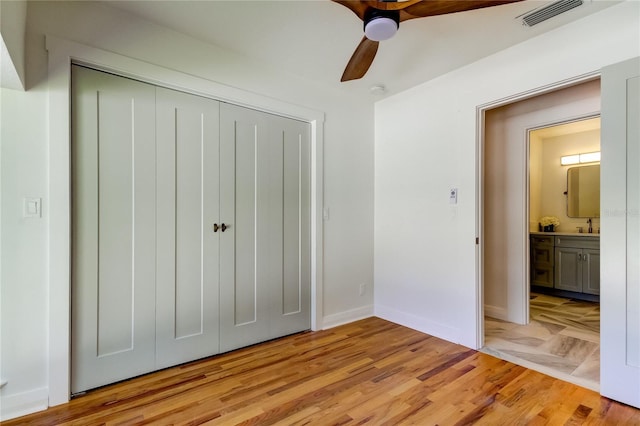 unfurnished bedroom featuring connected bathroom, ceiling fan, sink, light hardwood / wood-style flooring, and a closet