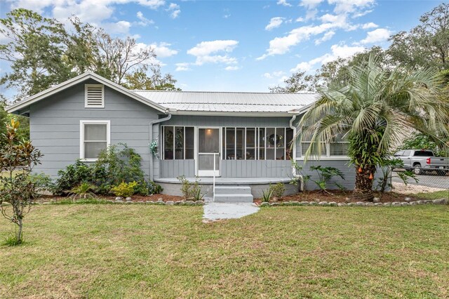 ranch-style home with fence, metal roof, a front yard, and a sunroom
