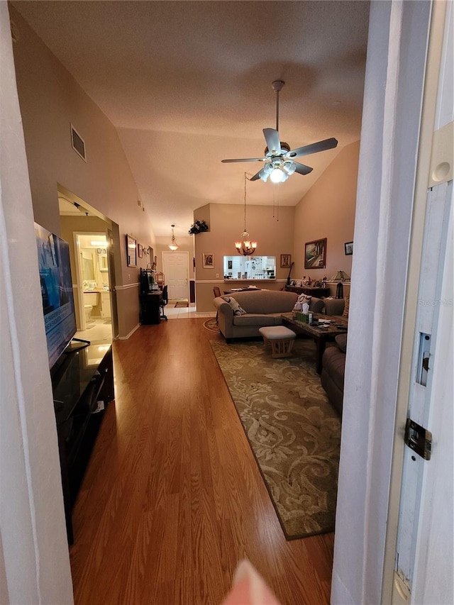 living room with vaulted ceiling, ceiling fan with notable chandelier, and hardwood / wood-style floors