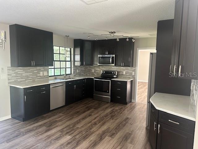 kitchen featuring a textured ceiling, appliances with stainless steel finishes, dark hardwood / wood-style floors, and backsplash