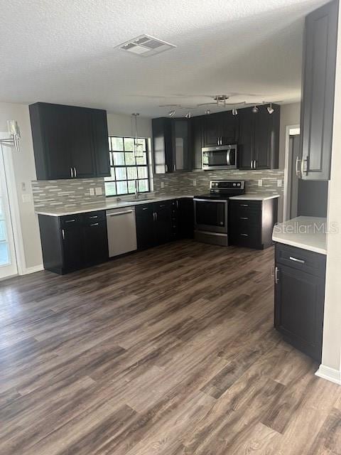 kitchen with appliances with stainless steel finishes, a textured ceiling, tasteful backsplash, and dark hardwood / wood-style flooring