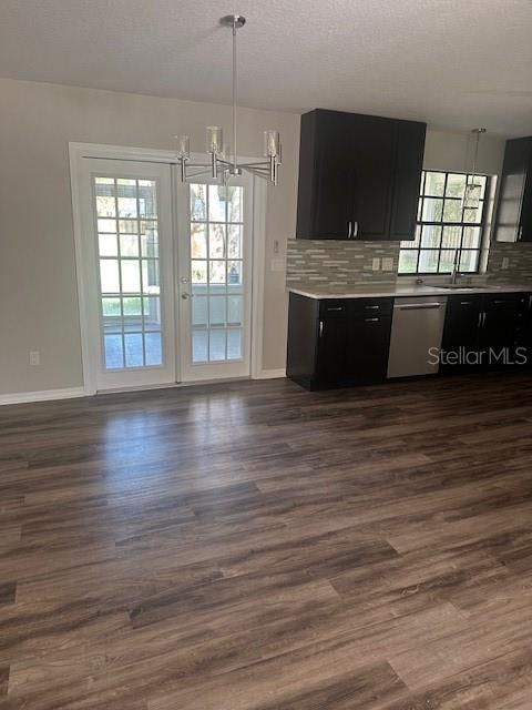 kitchen with decorative backsplash, stainless steel dishwasher, dark wood-type flooring, pendant lighting, and a notable chandelier