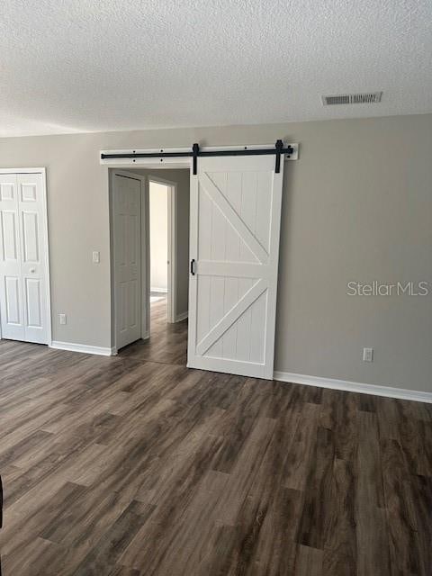 empty room featuring a textured ceiling, a barn door, and dark hardwood / wood-style floors