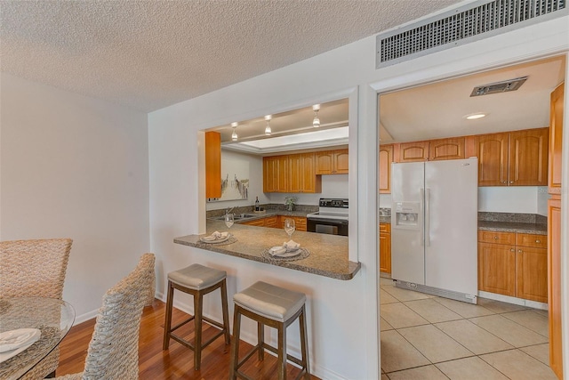 kitchen featuring white refrigerator with ice dispenser, kitchen peninsula, a breakfast bar, a textured ceiling, and black / electric stove