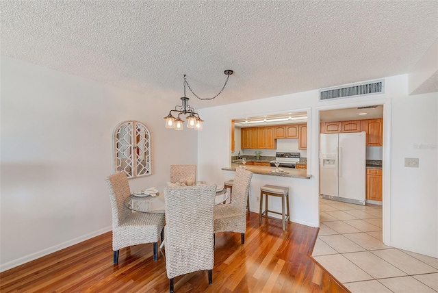 dining area featuring a textured ceiling, light wood-type flooring, and a notable chandelier