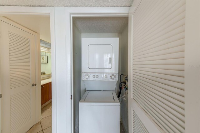 laundry area featuring light tile patterned floors, a textured ceiling, and stacked washer and dryer