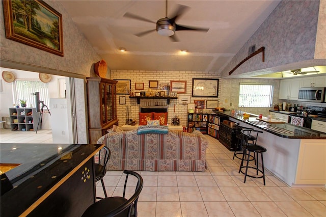 interior space with appliances with stainless steel finishes, a kitchen bar, ceiling fan, white cabinets, and brick wall