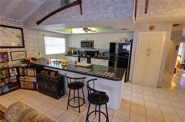 kitchen with kitchen peninsula, black appliances, a kitchen bar, light tile patterned floors, and white cabinetry