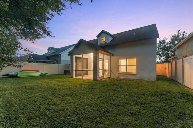 back house at dusk featuring a sunroom and a lawn