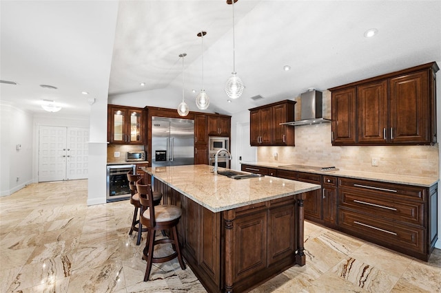 kitchen with wall chimney range hood, tasteful backsplash, a center island with sink, vaulted ceiling, and built in appliances