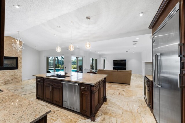 kitchen featuring lofted ceiling, dark brown cabinets, hanging light fixtures, appliances with stainless steel finishes, and a kitchen island with sink