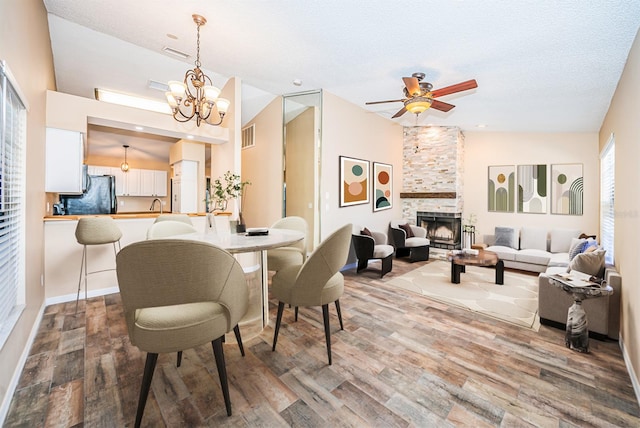 dining room featuring a textured ceiling, ceiling fan with notable chandelier, wood-type flooring, and a fireplace