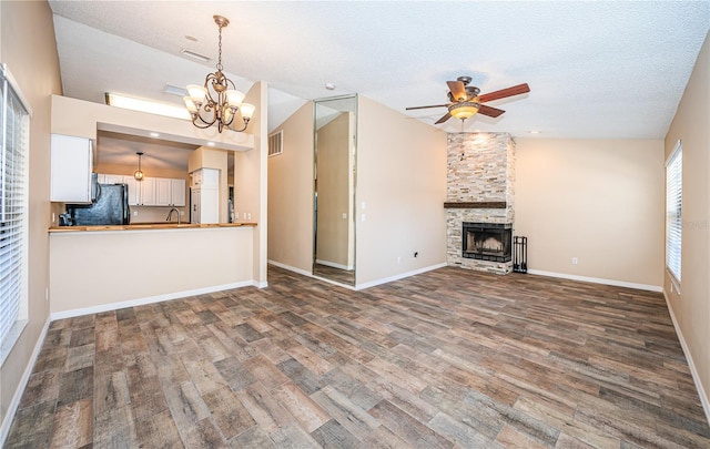 unfurnished living room featuring a stone fireplace, hardwood / wood-style floors, vaulted ceiling, a textured ceiling, and ceiling fan with notable chandelier