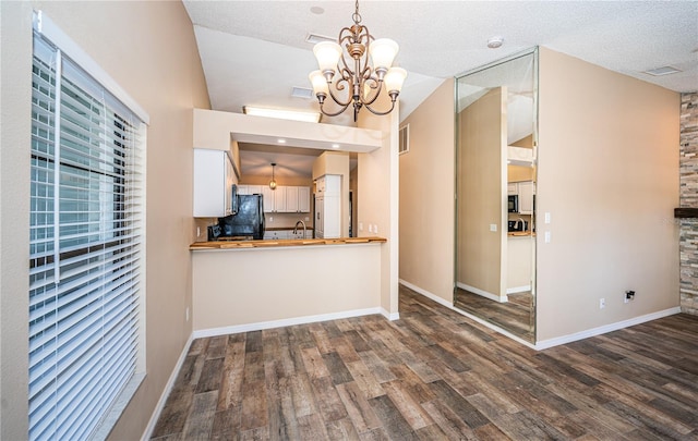 kitchen featuring pendant lighting, hardwood / wood-style floors, vaulted ceiling, a textured ceiling, and a notable chandelier